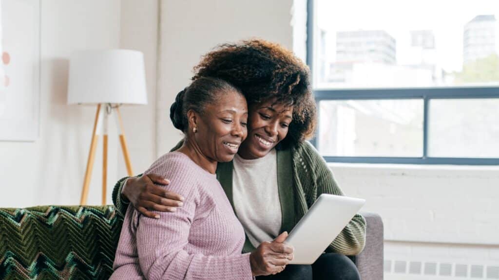 Two women sitting comfortably on a couch, focused on a tablet